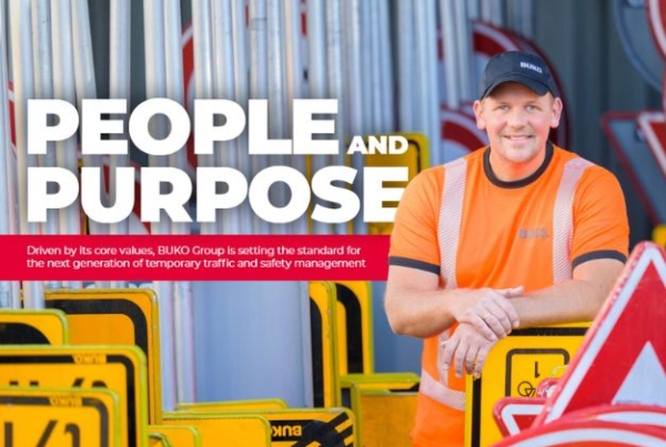 BUKO worker in hi-visibility orange standing among road safety signs.
