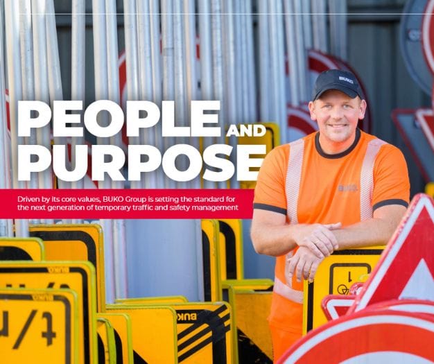 BUKO worker in hi-visibility orange standing among road safety signs.